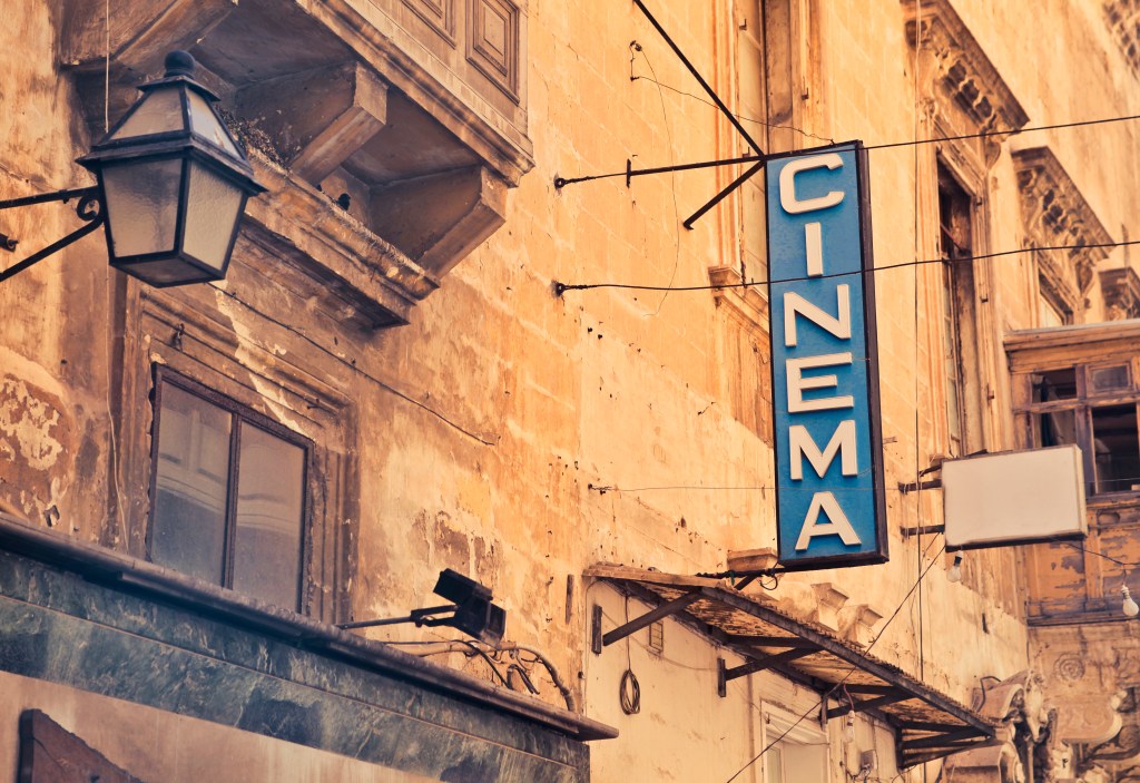 Blue sign against brown wall reads "Cinema" used to highlight the similarity between credits at the movies and books and publishing credits pages.