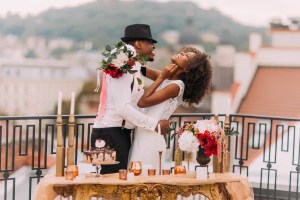 Woman and man in wedding attire laughing next to table; man wearing hat and woman holding bouquet. Romance novels typically end with happily ever after.