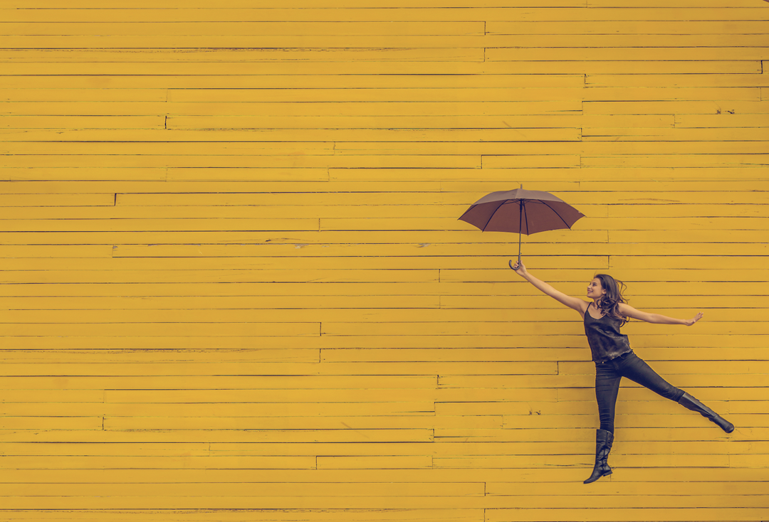 Background of yellow wood with brown-haired woman wearing black holding a brown umbrella.