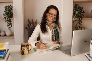 Cortni Merritt, MA, editor and writer, seated in front of her laptop, wearing reading glasses and taking notes. 