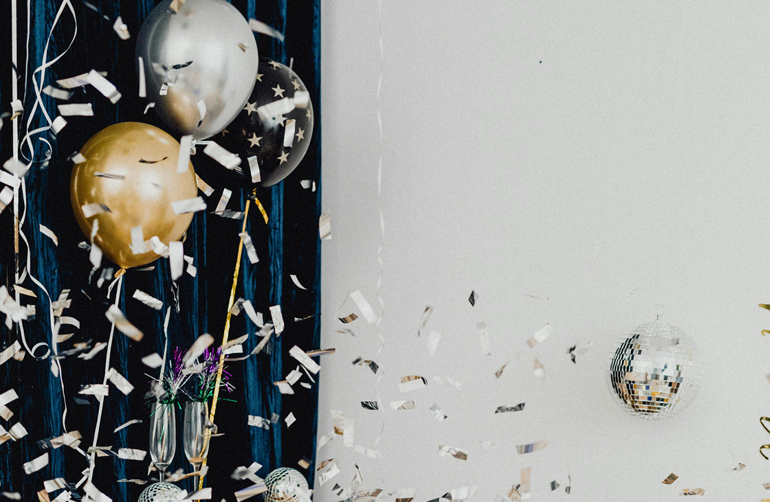 Silver and gold balloon and confetti against a black and white background; celebration theme.